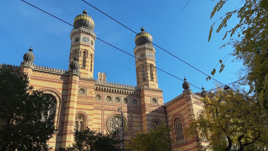 Main facade of the Dohany Street Synagogue, or Great Synagogue built in 19th-century with two towers with domes at autumn sunny morning, Budapest, Hungary, view from the street while panning 
