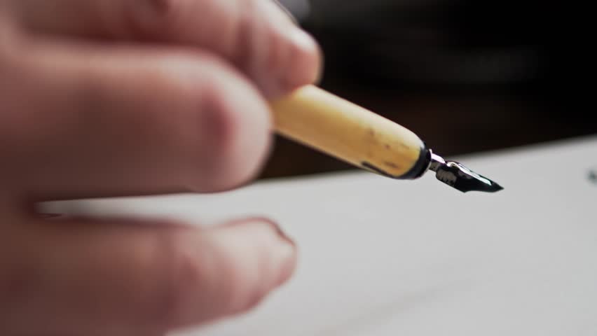 Calligraphy artist uses black ink dipper pen to draw stylised letter scroll