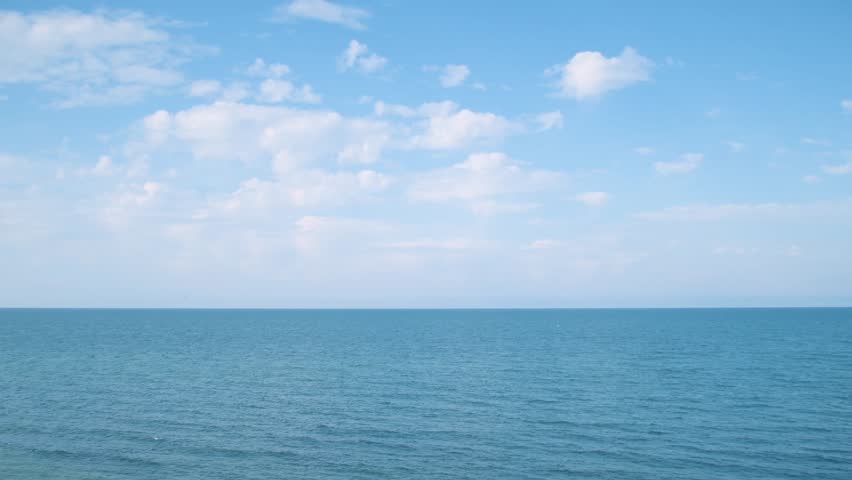 Vast expanse of clear, pale blue sky with horizon line over the sea. Serene and expansive view, embodying tranquility and openness.