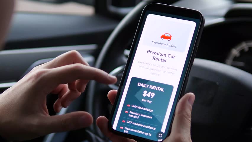 Closeup of a mans hands in a parked car completing a vehicle rental booking through a mobile application. The efficient process - from reviewing rental terms and pricing to receiving instant booking