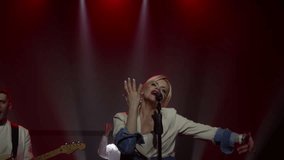 Female vocalist in denim jacket and white platform boots performing with male guitarist on professional stage with red theatrical lighting, energetic live music concert. - Powered by Shutterstock - Get 15% off with code: PIKWIZARD15