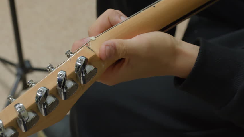 Close up of hand turning chrome tuning pegs on wooden guitar headstock, adjusting strings, metal machine heads, natural maple wood finish, neutral background, music preparation concept. - Powered by Shutterstock - Get 15% off with code: PIKWIZARD15