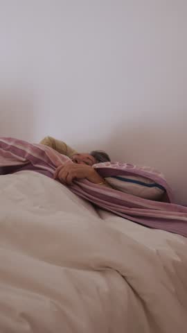 Elderly woman gently getting up from bed, relaxing muscles while preparing for her daily routine in comfortable bedroom setting