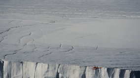 An orange helicopter surveys the towering face of a vast glacier, tracing the brink of an immense ice cliff as networks of crevasses spread across the frozen plateau - Powered by Shutterstock - Get 15% off with code: PIKWIZARD15