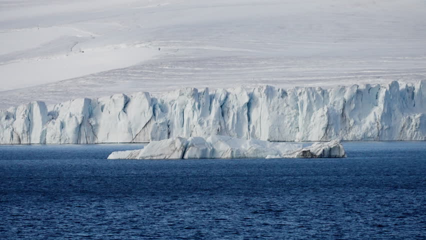 Vast polar shoreline with a drifting iceberg in deep blue water before a towering calving glacier, icy cliffs, and a frozen coast, capturing stark serenity and remote isolation.