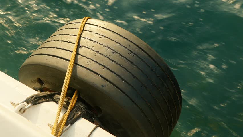 Large Boat Fender Tire With Rope Tied On Deck Over Turquoise Water
