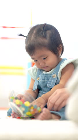 Asian toddler girl reaching colorful buttons on floor, exploring texture and shape, early sensory learning activity, curiosity and development, home family lifestyle, playful childhood Vertical