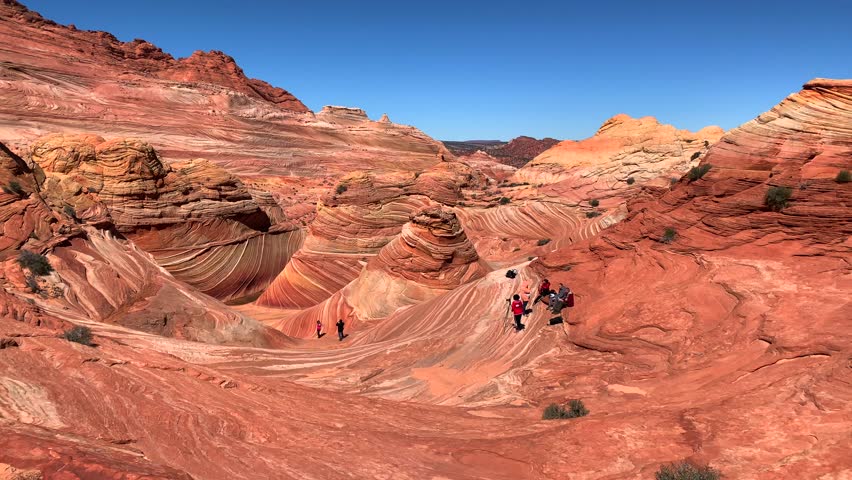 The Wave sandstone formation in Arizona, layered red rocks and unique desert landscape with hikers exploring the natural curves under a clear blue sky.