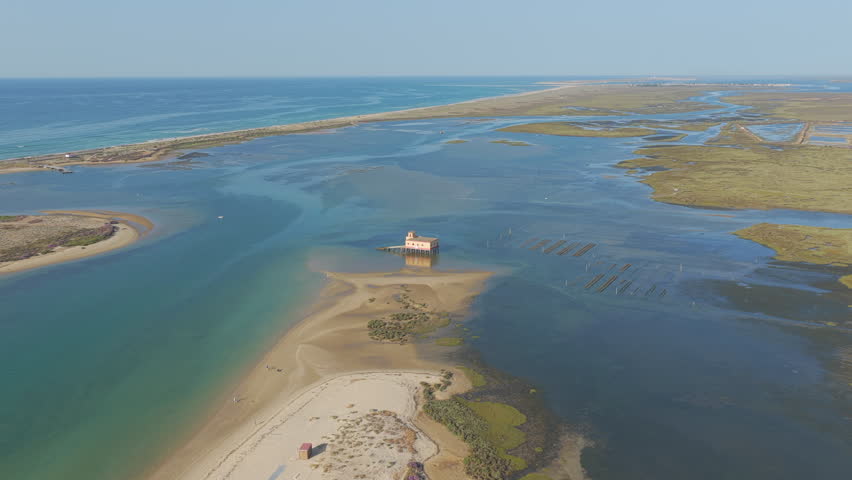 Descending aerial view of Fuzeta lagoon with rescue station and winding sandbank.