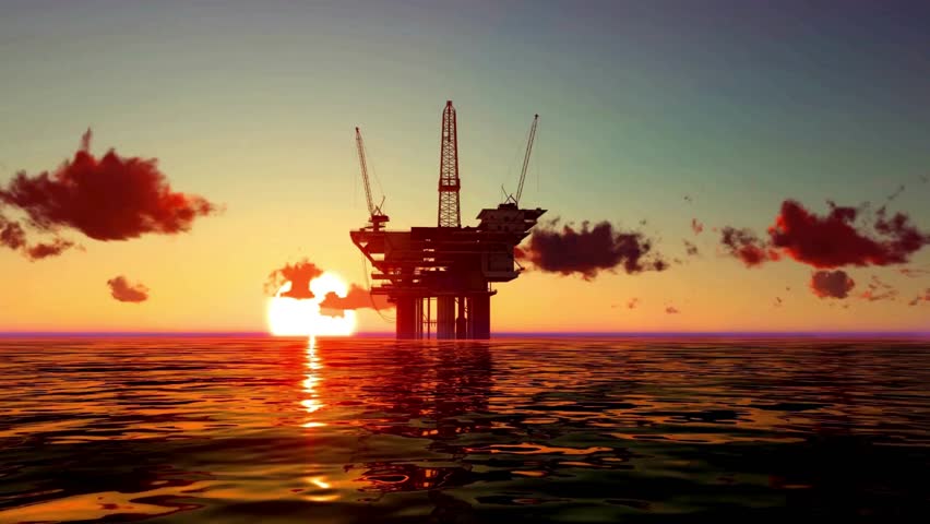 Glistening sun sets behind oil rig located in open waters, casting warm hues across calm ocean. Industrial structure stands tall against vibrant sky, highlighting energy industry at day's end.