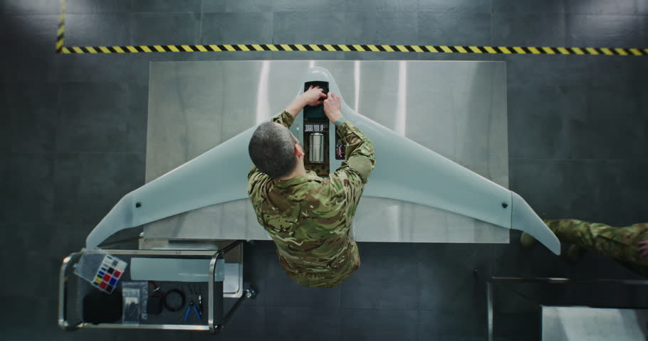 Engineer in Military Uniform Assembling Unmanned Aerial Vehicle. Man in Camouflage, Working on Internal Components of Fixed Wing UAV. Concept Precision of Military Technology Production. Top View.