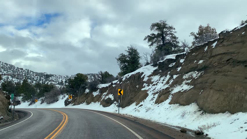 Snowy mountain highway winding through pine forests under a bright winter sky — a quiet moment on the road between Arizona and Utah.