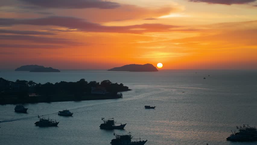 Breathtaking aerial view of the sun setting over the sea and distant islands at Kota Kinabalu Waterfront harbour filled with silhouetted fishing boats in Sabah Malaysia