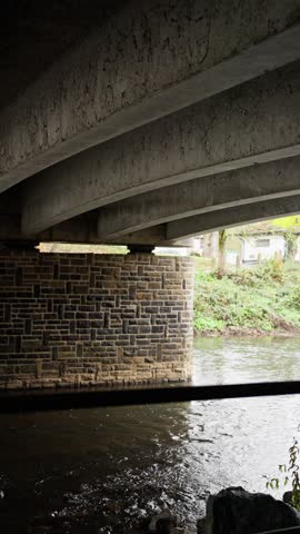 peaceful water and stone harbor landscape, tranquil canal beneath stone arches reflecting subtle water movement, relaxing scene of concrete underpass over river with mosscovered banks