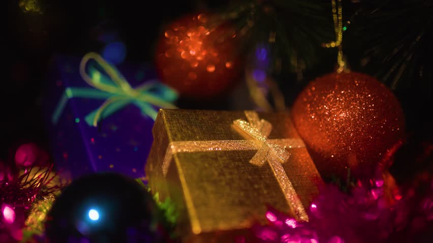 Close up golden gift box tied with a bow against the background of an incredibly lovely glow of a garland. Christmas toys and holiday atmosphere. Selective focus.