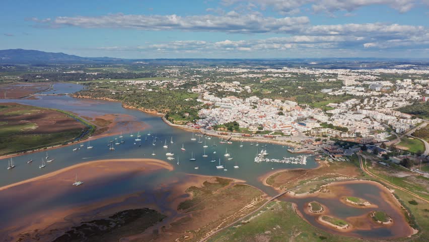 Alvor aerial view drone aerial estuary view over alvor showcasing winding river, tidal mudflats and moored boats beside whitewashed town and marshy sandbanks under clear blue sky, serene