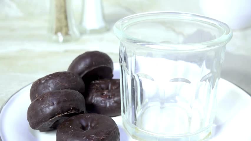 Fresh Milk stream filling clean Glass. Glazed chocolate donuts lie on white plate next to it. Perfect, tasty breakfast indulgence for Food concepts.