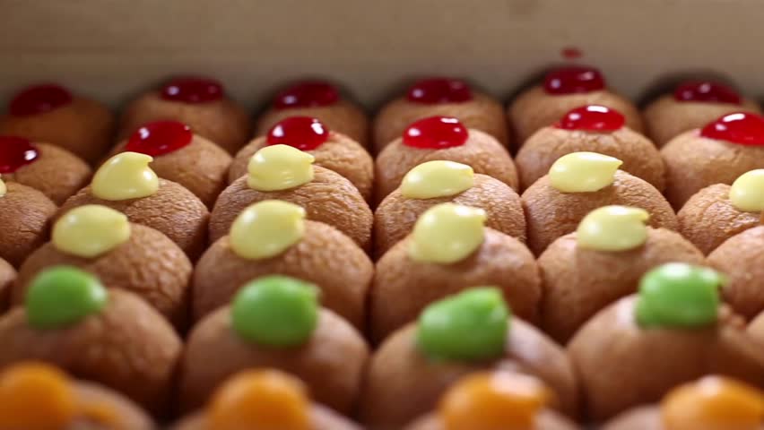 Close-up view shows a tempting array of pastries topped with colorful icing and fruit pieces in a bakery setting, inviting customers to indulge.