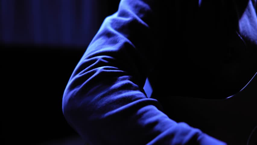 A guitarist plays an acoustic guitar on stage under flickering spotlights