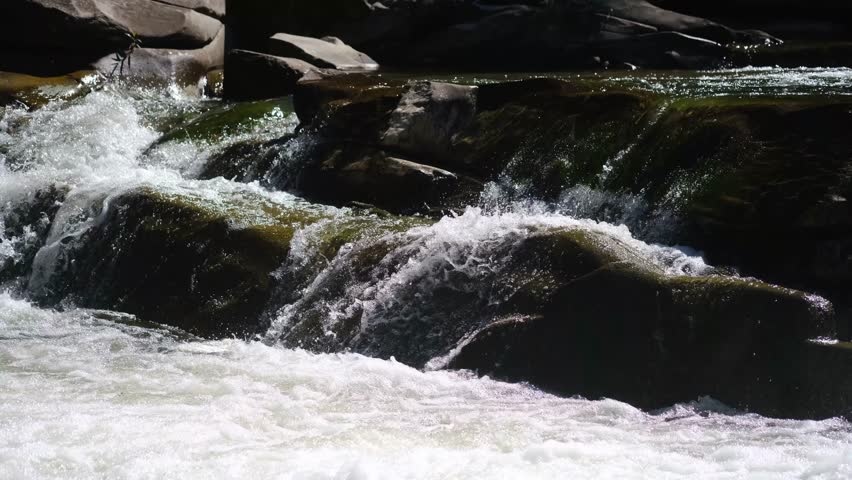 Clear water flowing over smooth rocks in a natural river rapids with white foam and spray