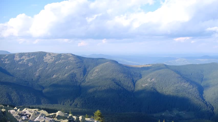 Deep green mountain ranges stretch towards a hazy horizon under a bright sky with scattered clouds.