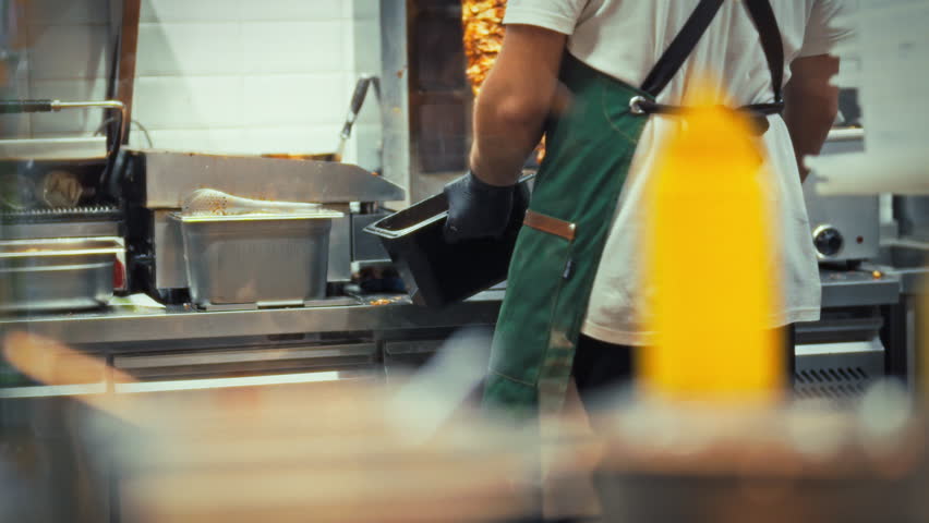 In a busy fast food restaurant kitchen, chefs focus on assembling orders quickly. They chop ingredients and cook meat, ensuring customers receive meals promptly during peak hours