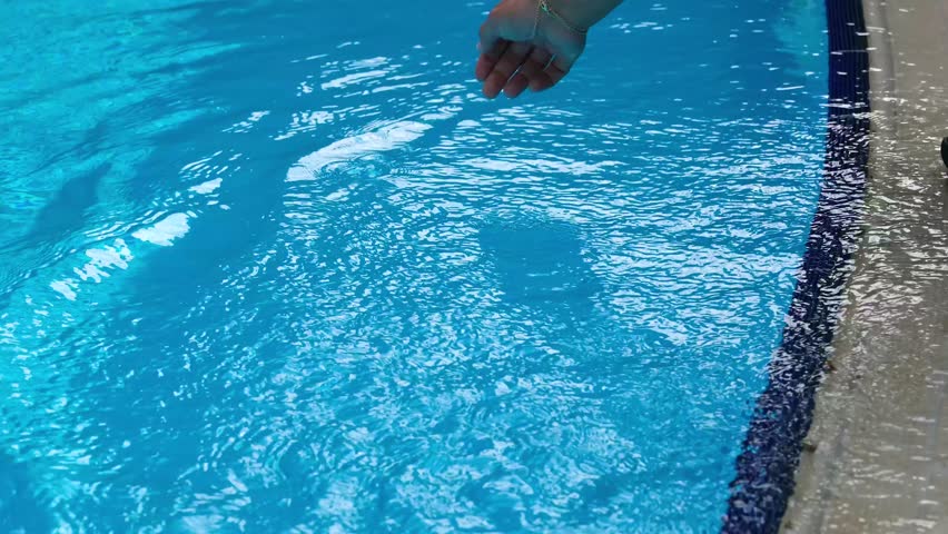 A young girl is playing with the water at the edge of the pool, The scene is captured in slow motion, emphasizing the delicate movement of her hand through the water.