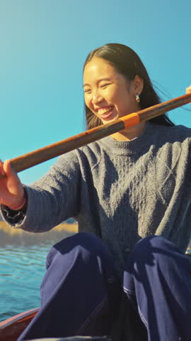 Two persons in cozy sweaters canoe on a serene lake, smiling and enjoying a peaceful outdoor adventure. The clear blue sky and calm water enhance the relaxing, active lifestyle scene.