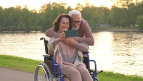 Senior couple woman in wheelchair caregiver old man making selfie enjoying walking. Elderly family man supporting embracing woman in chair for people with disability taking photo. Rehabilitation - Powered by Shutterstock - Get 15% off with code: PIKWIZARD15