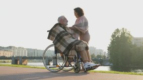 Old man in wheelchair walking with caregiver senior woman in park. Elderly family couple woman supporting taking care of paralyzed man in chair for people with disability outdoor. Rehabilitation - Powered by Shutterstock - Get 15% off with code: PIKWIZARD15