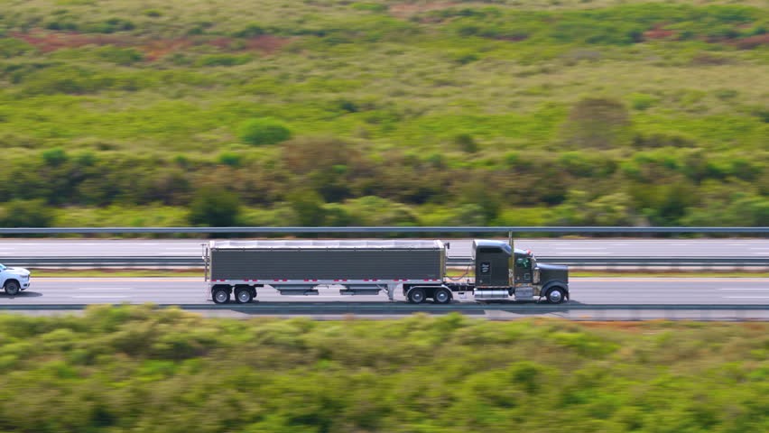 Lorry semi truck delivering cargo in hauling trailer on multilane American freeway.