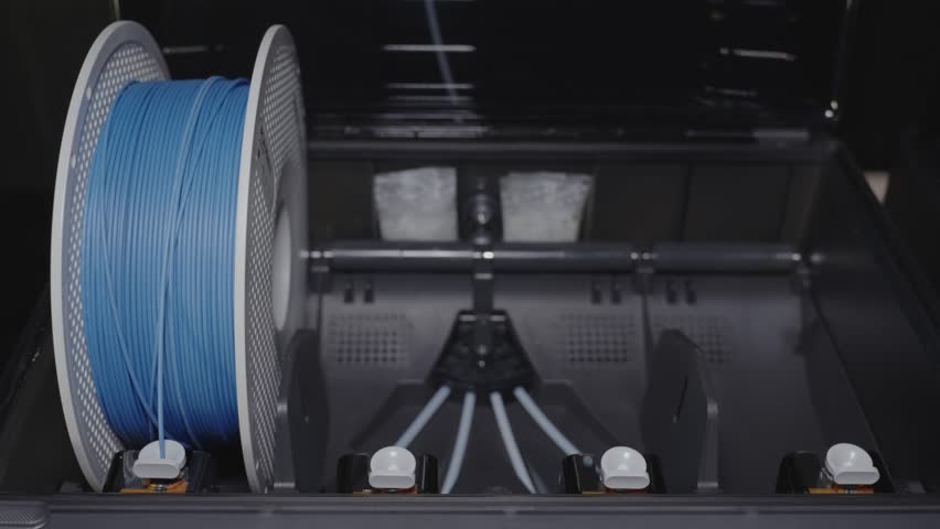 The 3D printer operator installs spools of plastic that will be fed into the extruder nozzle and exit the hot end