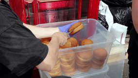 Vendor using tongs to organize baked buns, Food vendor quickly arranging fresh bread products outdoors, Market stall worker swiftly stacking bakery items into containers for event serving - Powered by Shutterstock - Get 15% off with code: PIKWIZARD15