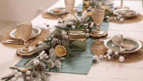 A detailed 4K view of an elegant rustic Christmas table setting featuring frosted greenery, white berries, dried orange slices, and a small gold house. - Powered by Shutterstock - Get 15% off with code: PIKWIZARD15