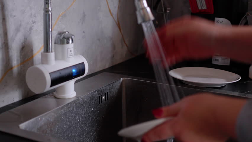 Hands of a woman washing a plate under running water in a modern kitchen sink, showcasing the cleaning process with a close-up camera zooming in on the action