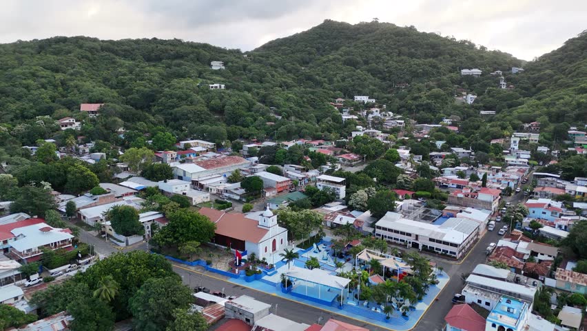 Explore beautiful village in coastal Nicaragua surrounded by hills and greenery, showcasing vibrant homes and local culture.