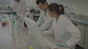 Center man leaning to screen, moving to scope; woman tapping; left pipetting; overlay over lab team. Researchers, laboratory, microscope, touchscreen, pipette, gloves, goggles - Powered by Shutterstock - Get 15% off with code: PIKWIZARD15