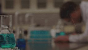 Man leaning over bench, frames unfolding and teal flask, formulas appearing and showing math in lab. Researcher, laboratory, glassware, liquid, trays, science, education - Powered by Shutterstock - Get 15% off with code: PIKWIZARD15