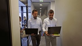Two business coworkers walk through a modern office hallway, engaging in a focused discussion while reviewing work on their laptops. - Powered by Shutterstock - Get 15% off with code: PIKWIZARD15