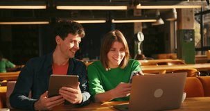Young man and woman working together in cozy cafe, using laptop, tablet and smartphone to discuss their project, sharing ideas and smiling while enjoying warm atmosphere. Online technology concept - Powered by Shutterstock - Get 15% off with code: PIKWIZARD15