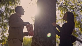 A diverse young couple shares playful moments, tossing popcorn by a large tree in a beautiful, sun-dappled park. They are laughing and enjoying their time together outdoors. - Powered by Shutterstock - Get 15% off with code: PIKWIZARD15