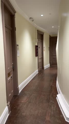 Long, quiet corridor with wood doors and cream walls in a vintage building. Clean lines and curved trim lead the eye down the passage.