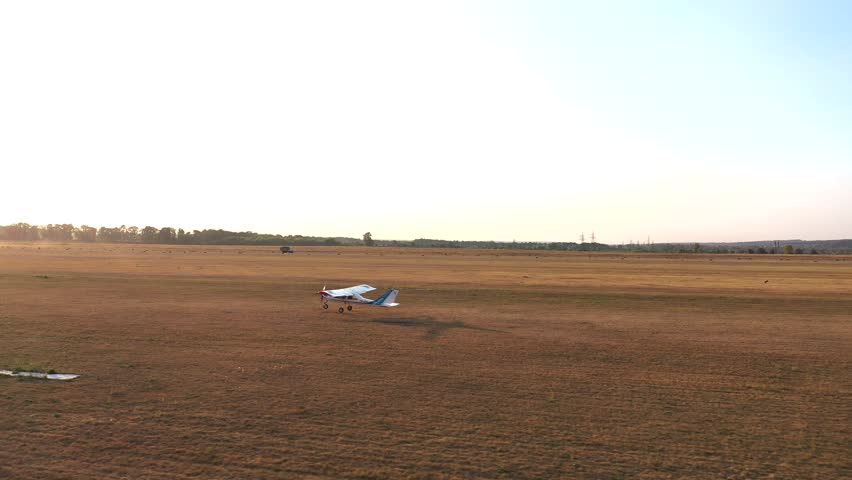Small airplane takes off from grass airstrip of small airport. Lightweight plane move at rural runway and starting flight. Ultralight sport aircraft detach from airfield. Aviation concept. Aerial view