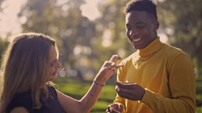 A cheerful multiethnic couple enjoys a tender and playful interaction with a small green plant in a beautiful, sunlit park. Their happy expressions capture a moment of love and connection. - Powered by Shutterstock - Get 15% off with code: PIKWIZARD15