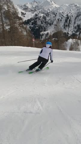 Experienced female skier carving down the groomed slope of a snowy alpine ski resort. Unrecognizable woman enjoys skiing during an active winter vacation in the beautiful mountains of Austrian Alps.