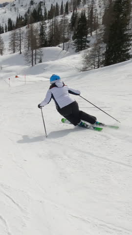 Experienced female skier carving down the groomed slope of a snowy alpine ski resort. Unrecognizable woman enjoys skiing during an active winter vacation in the beautiful mountains of Austrian Alps.