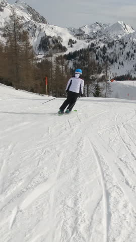 Following unknown lady skiing on a groomed ski track at picturesque alpine resort. Experienced female skier enjoys skiing during an active winter vacation among beautiful mountains of Austrian Alps.