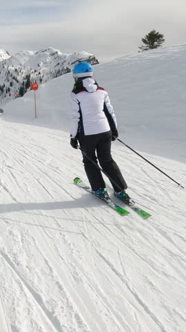 Following unknown lady skiing on a groomed ski track at picturesque alpine resort. Experienced female skier enjoys skiing during an active winter vacation among beautiful mountains of Austrian Alps.