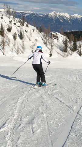 Sunny winter day with an experienced female skier skiing at alpine ski resort. Unrecognizable woman enjoys skiing during an active winter vacation in the beautiful mountains of Austrian Alps.