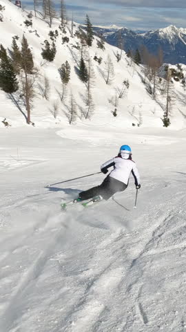 Sunny winter day with an experienced female skier skiing at alpine ski resort. Unrecognizable woman enjoys skiing during an active winter vacation in the beautiful mountains of Austrian Alps.